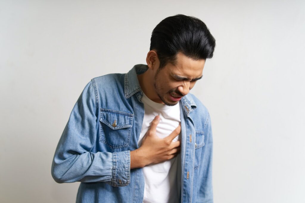 Young Asian man touching his chest where he feels pain due to heart attack problem.