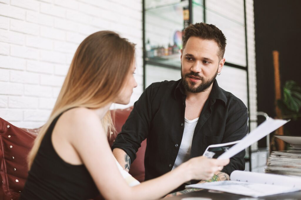 Professional tattooer discussing with girl new tattoo in studio